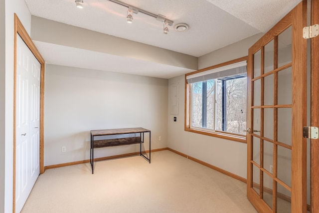 interior space featuring light carpet, baseboards, a textured ceiling, and track lighting