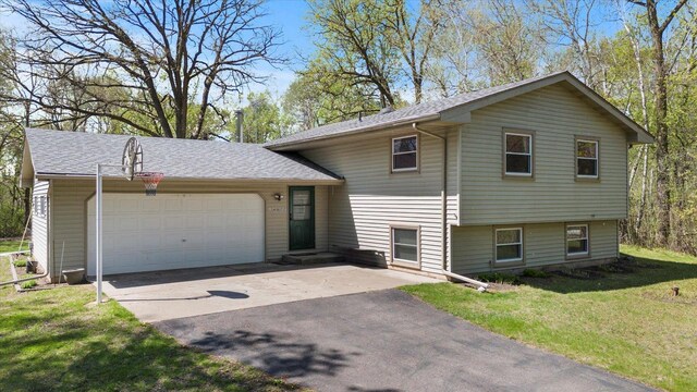 split level home featuring a garage, concrete driveway, a front lawn, and a shingled roof