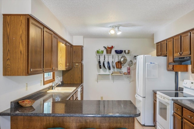 kitchen featuring white appliances, under cabinet range hood, a sink, a peninsula, and a textured ceiling