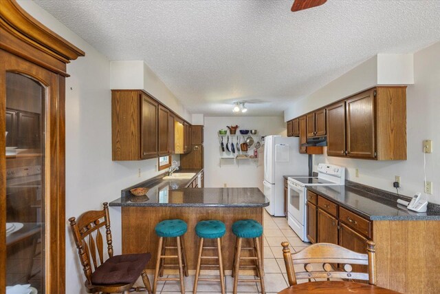 kitchen featuring electric range, a sink, a textured ceiling, a peninsula, and dark countertops