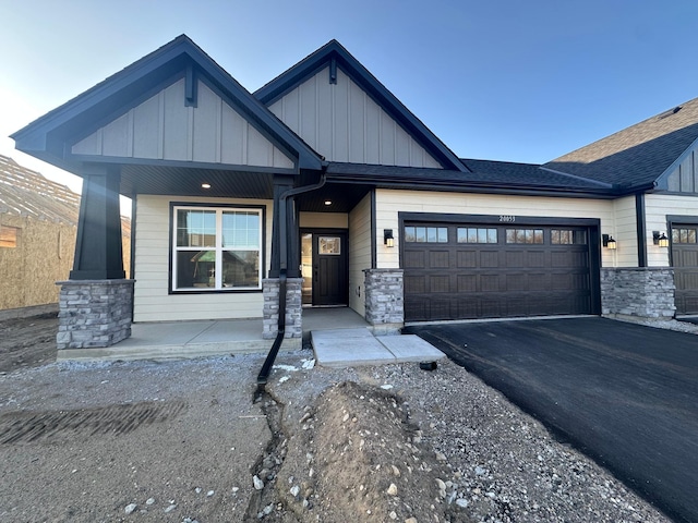view of front of home featuring board and batten siding, driveway, a porch, stone siding, and a garage