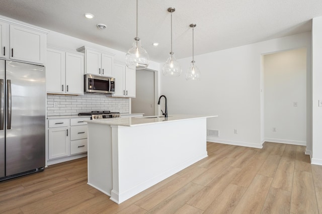 kitchen featuring a sink, light wood-style floors, a kitchen island with sink, backsplash, and appliances with stainless steel finishes