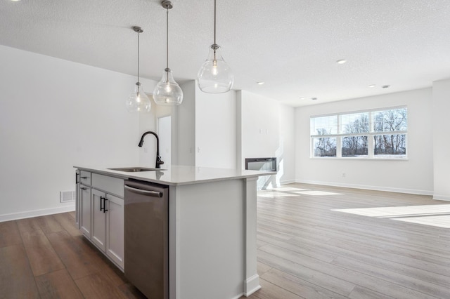 kitchen featuring stainless steel dishwasher, a sink, a textured ceiling, and light wood-style flooring