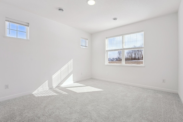 empty room with plenty of natural light, baseboards, and light colored carpet