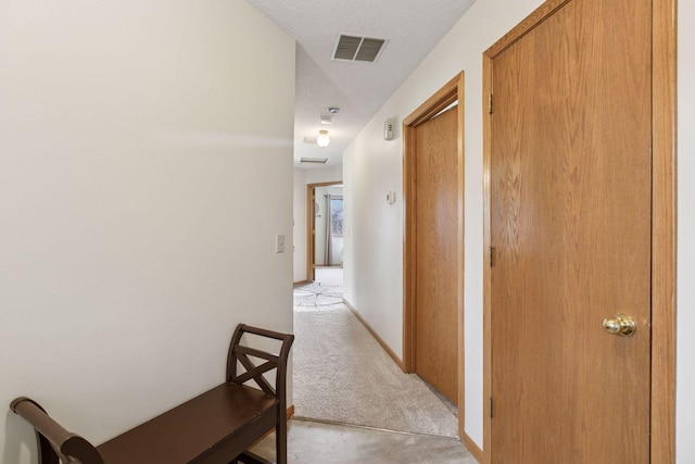 hallway with a textured ceiling, visible vents, and light colored carpet