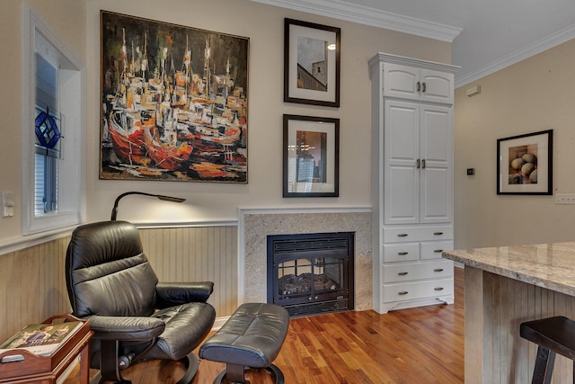 living area with crown molding, light wood-style flooring, a fireplace, and a wainscoted wall