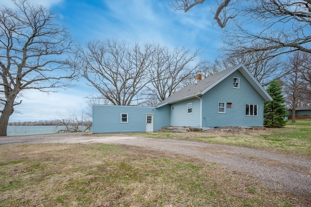 back of property featuring a water view, a lawn, a chimney, driveway, and roof with shingles