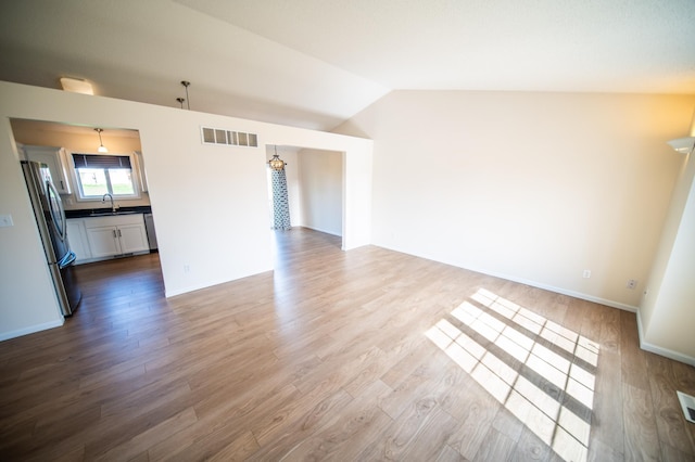 unfurnished living room featuring visible vents, wood finished floors, a sink, baseboards, and lofted ceiling