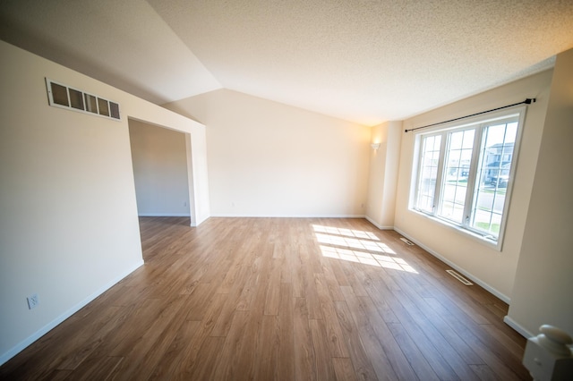 unfurnished room with lofted ceiling, wood finished floors, and visible vents