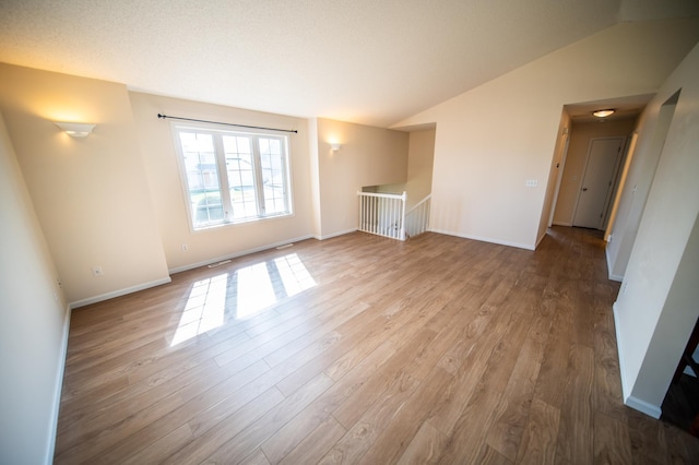 unfurnished living room with baseboards, wood finished floors, vaulted ceiling, and visible vents