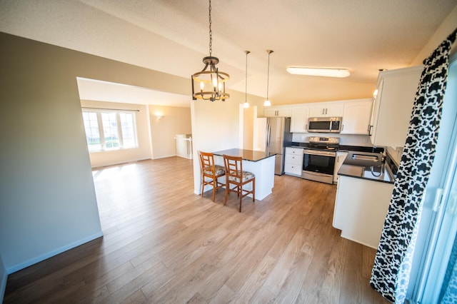 kitchen featuring dark countertops, appliances with stainless steel finishes, a sink, lofted ceiling, and a breakfast bar