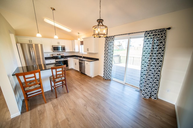 kitchen featuring dark countertops, appliances with stainless steel finishes, a sink, white cabinetry, and lofted ceiling