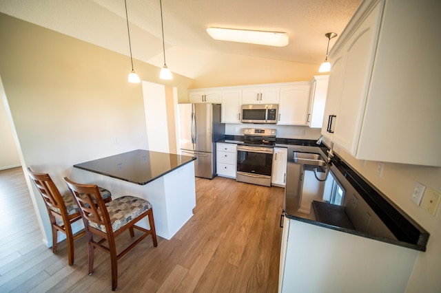 kitchen featuring dark countertops, white cabinetry, a sink, appliances with stainless steel finishes, and vaulted ceiling