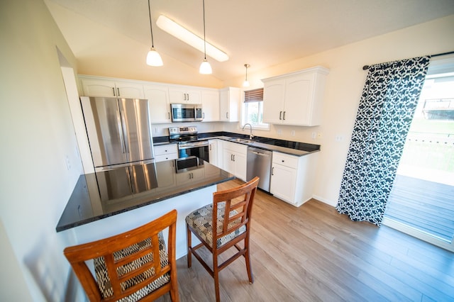 kitchen with a kitchen bar, a sink, white cabinets, lofted ceiling, and stainless steel appliances