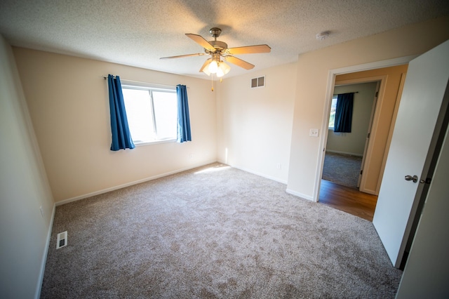 carpeted empty room featuring baseboards, ceiling fan, a textured ceiling, and visible vents
