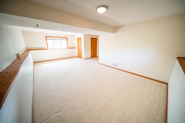 empty room featuring visible vents, carpet flooring, baseboards, and a textured ceiling