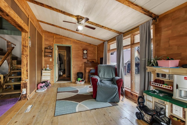 living area with lofted ceiling with beams, wooden walls, a ceiling fan, stairs, and hardwood / wood-style floors