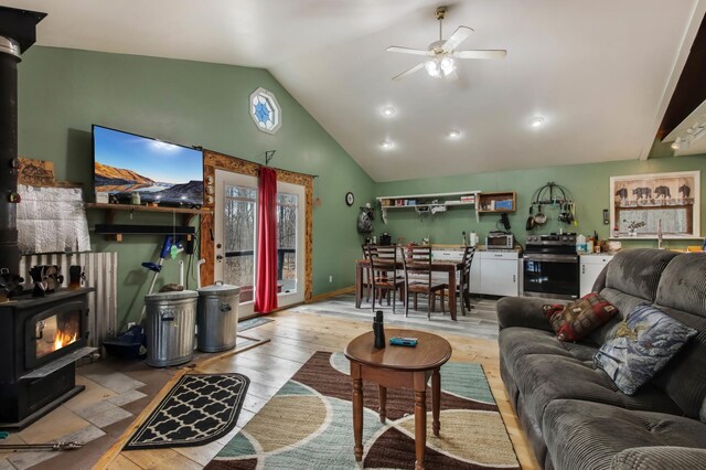living area with wood-type flooring, a wood stove, ceiling fan, and vaulted ceiling
