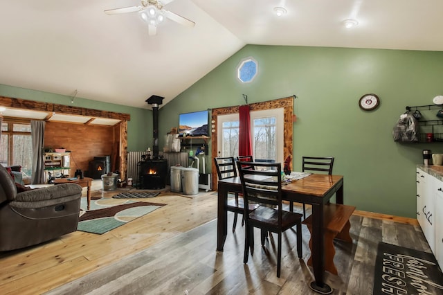 dining room with a wood stove, a ceiling fan, high vaulted ceiling, and wood finished floors