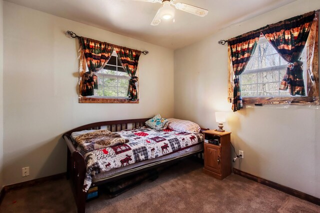 bedroom with baseboards, multiple windows, dark carpet, and a ceiling fan