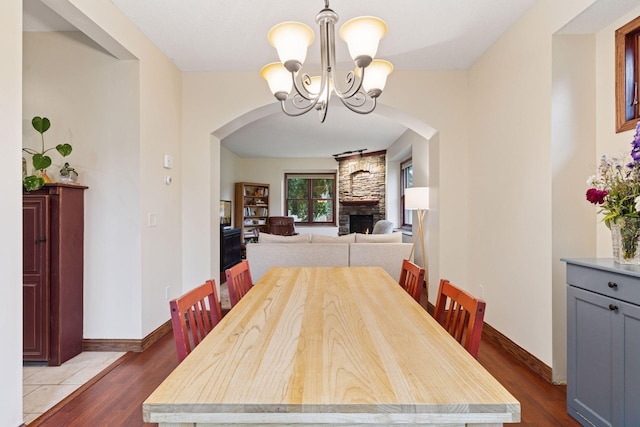 1584 Merrill St, Saint Paul, MN 55108 - dining room featuring arched walkways, a chandelier, dark wood-type flooring, and a stone fireplace