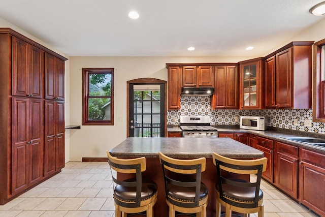 1584 Merrill St, Saint Paul, MN 55108 - kitchen featuring stainless steel stove, white microwave, reddish brown cabinets, decorative backsplash, and recessed lighting