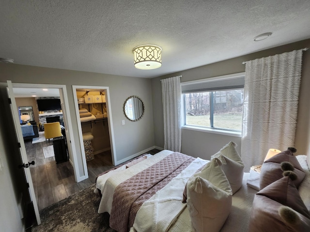 bedroom featuring baseboards, a textured ceiling, a walk in closet, and wood finished floors