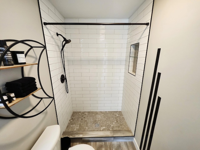 bathroom with toilet, wood finished floors, and a stall shower