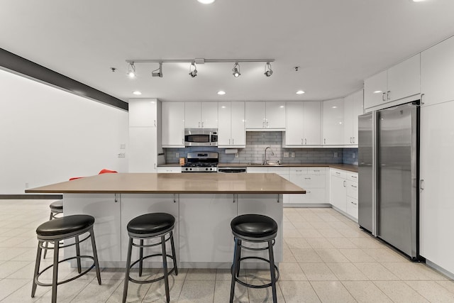 kitchen featuring white cabinets, a breakfast bar, a sink, stainless steel appliances, and tasteful backsplash