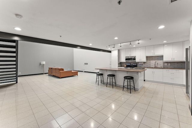 kitchen featuring open floor plan, a kitchen breakfast bar, white cabinets, backsplash, and stainless steel appliances