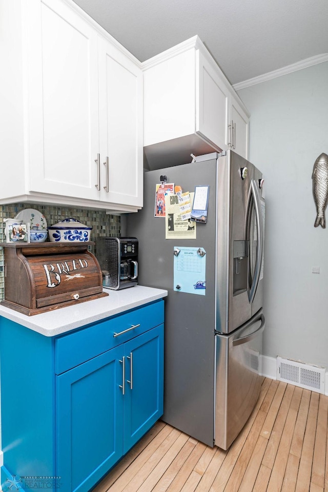 kitchen with light wood-style flooring, ornamental molding, visible vents, blue cabinets, and stainless steel fridge with ice dispenser