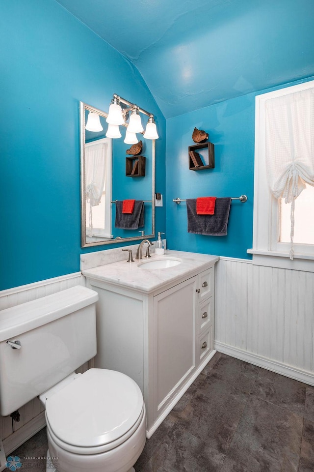 bathroom featuring vaulted ceiling, vanity, toilet, and wainscoting