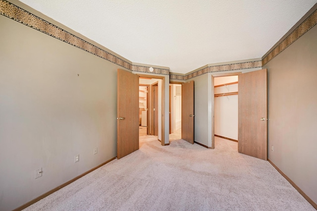 unfurnished bedroom with a walk in closet, baseboards, a closet, and light colored carpet