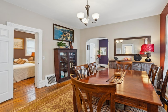 dining space featuring a chandelier, arched walkways, light wood finished floors, and visible vents