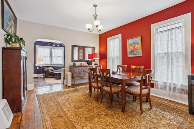 dining space with baseboards, arched walkways, a chandelier, and wood finished floors