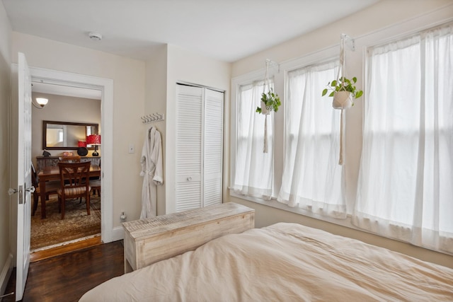 bedroom featuring a closet, baseboards, multiple windows, and dark wood finished floors