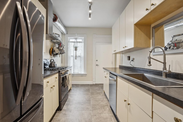 kitchen featuring baseboards, dark countertops, wall chimney exhaust hood, stainless steel appliances, and a sink