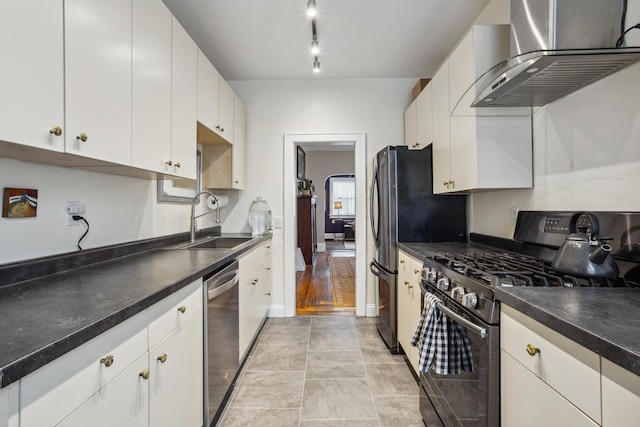 kitchen featuring wall chimney range hood, dark countertops, white cabinets, stainless steel appliances, and a sink