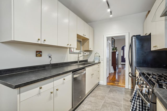kitchen with track lighting, a sink, dark countertops, appliances with stainless steel finishes, and white cabinetry