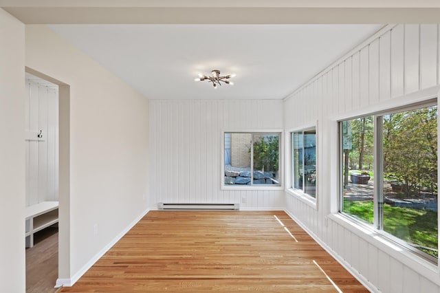unfurnished sunroom featuring a baseboard heating unit, wood finished floors, a chandelier, and baseboards