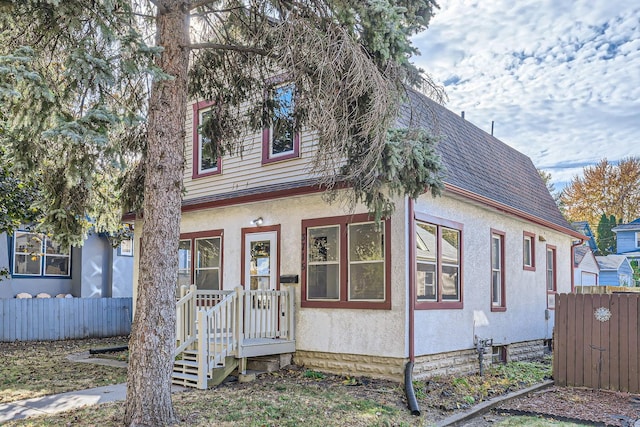 view of front of property featuring stucco siding, fence, and a shingled roof