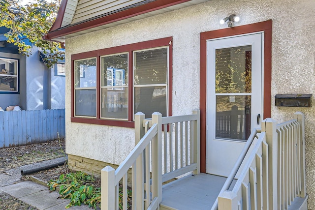 doorway to property with stucco siding and fence
