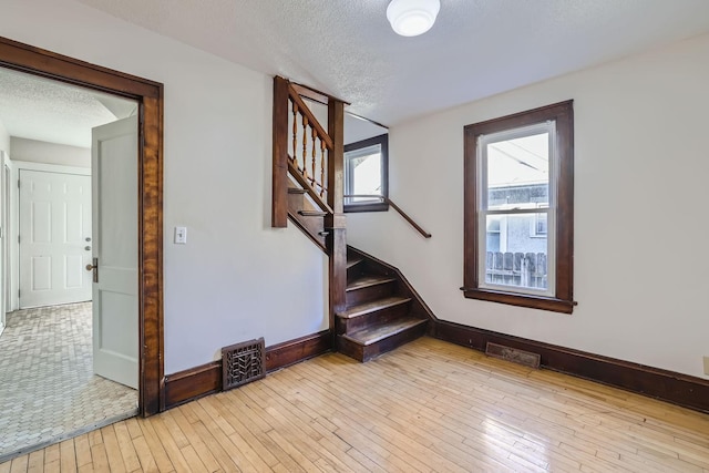 staircase featuring hardwood / wood-style floors, visible vents, baseboards, and a textured ceiling