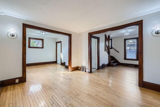 interior space with ornamental molding, light wood-type flooring, stairway, and baseboards