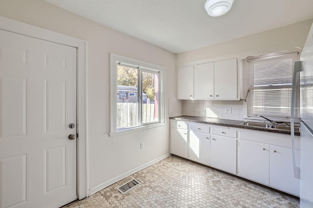 kitchen featuring white cabinets, visible vents, a sink, dark countertops, and baseboards