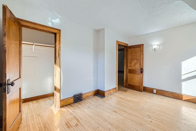 unfurnished bedroom featuring light wood-type flooring, baseboards, visible vents, and a textured ceiling
