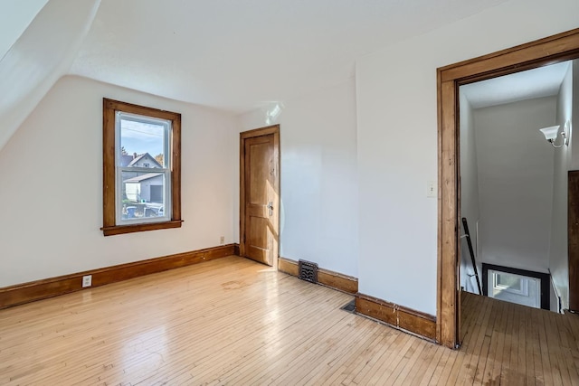 additional living space with light wood finished floors, visible vents, baseboards, and lofted ceiling