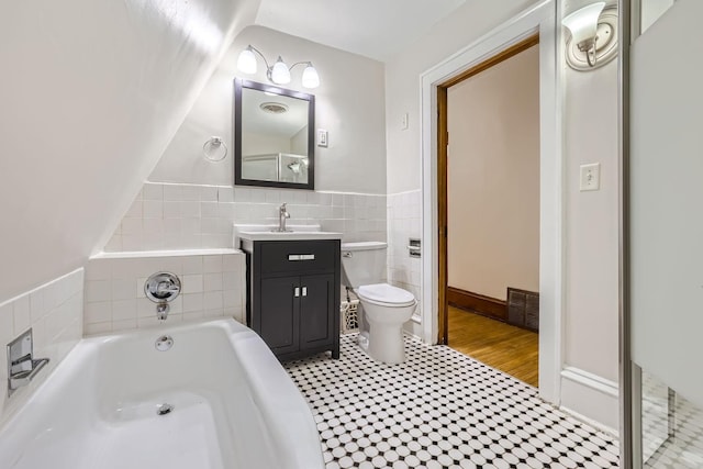 full bath with visible vents, a bath, tile walls, toilet, and vanity