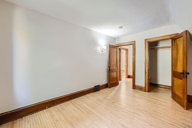 unfurnished bedroom featuring a closet, baseboards, light wood finished floors, and a textured ceiling