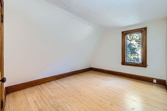 spare room with light wood-type flooring, baseboards, vaulted ceiling, and a textured ceiling
